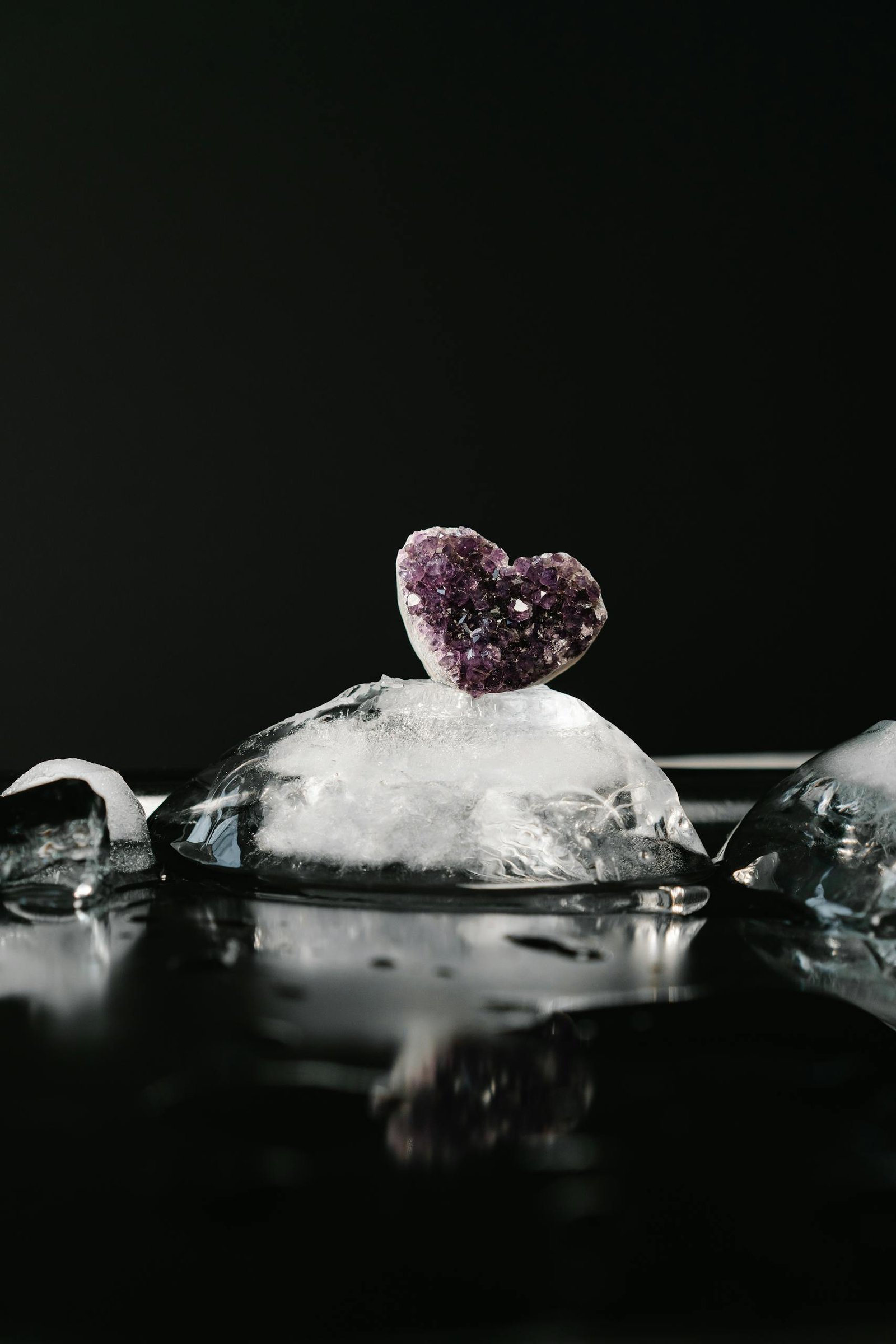 A heart-shaped amethyst crystal atop melting ice against a dark background.