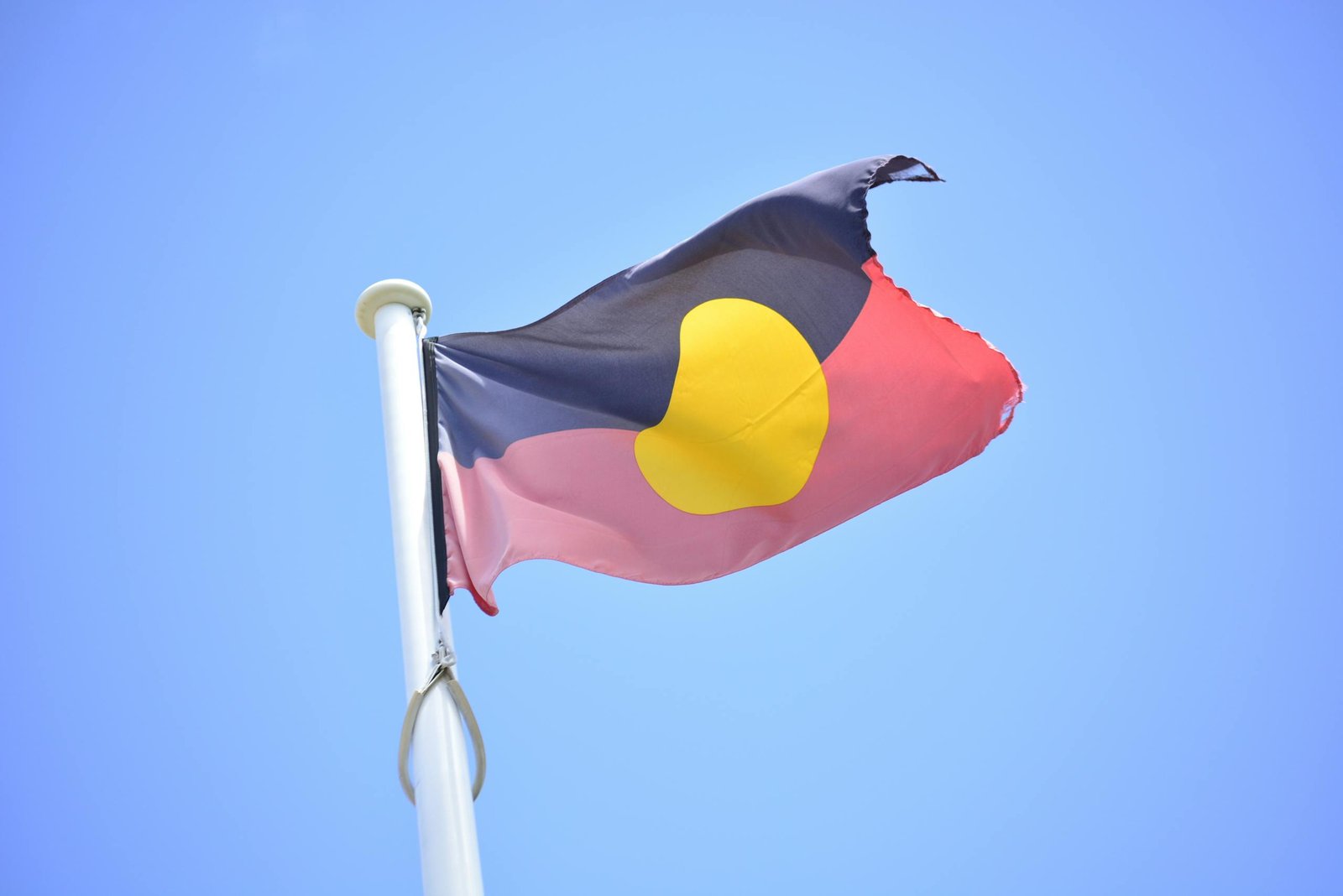 Australian Aboriginal flag waving against a clear blue sky, symbolizing culture and heritage.