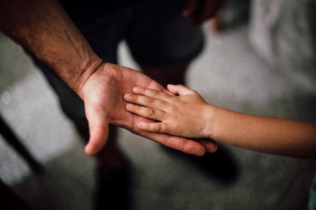 Close-up of a child's hand resting gently on a man's hand, symbolizing love and support.