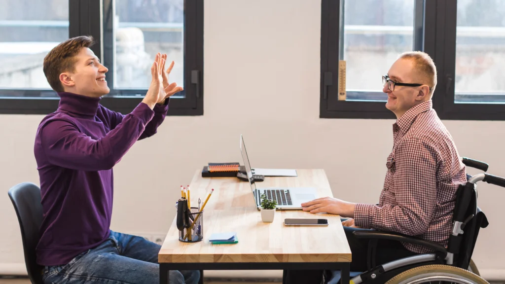 A high-angle shot of a meeting between a consultant and a client in a wheelchair. The consultant smiles while holding a clipboard, demonstrating the face-to-face communication essential for successful NDIS coordination and plan management.